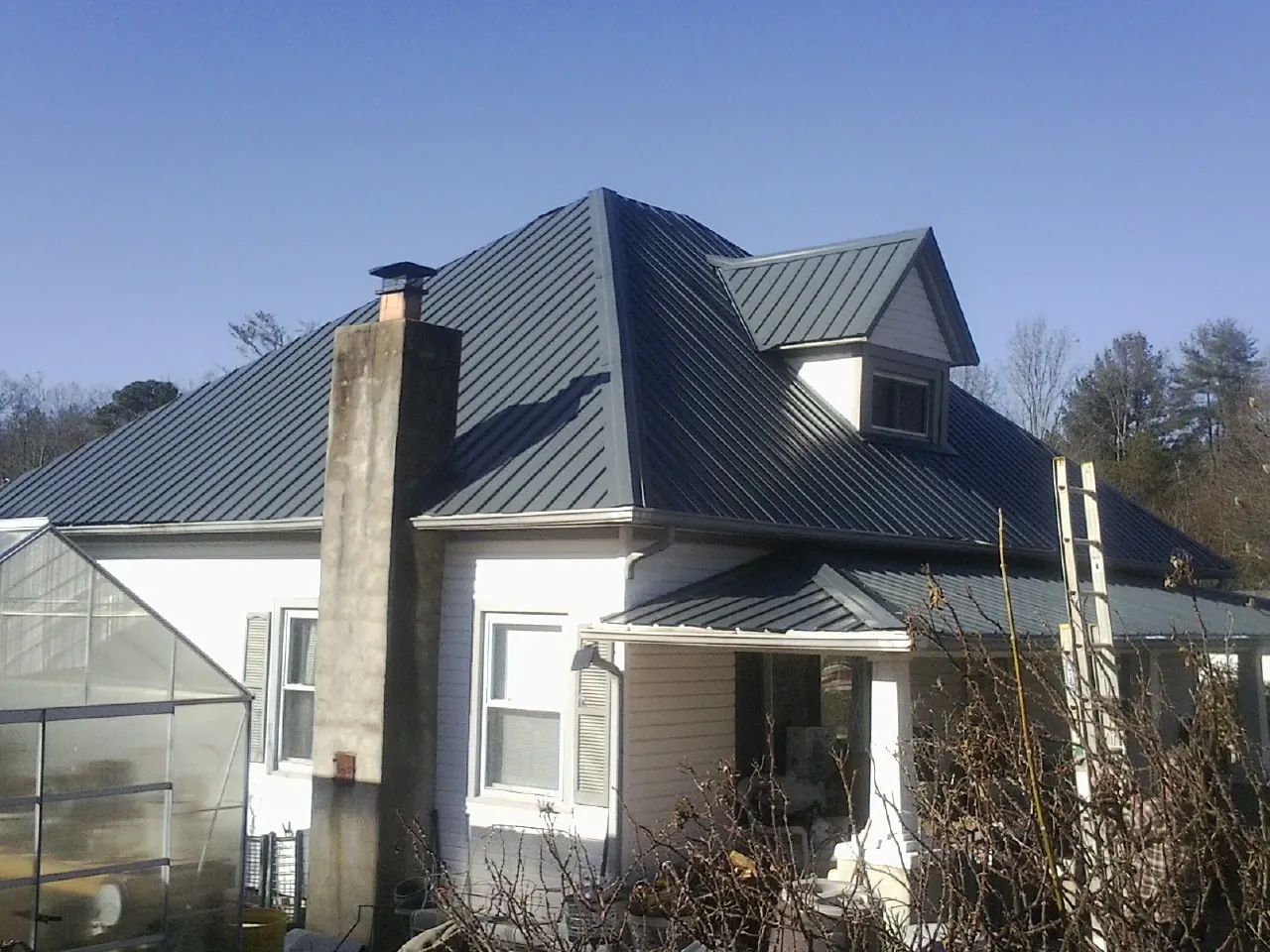 Dark blue standing seam metal roof on a white farmhouse with dormer — Slate & Tile Roof Repair by Roofing Brothers in San Andreas