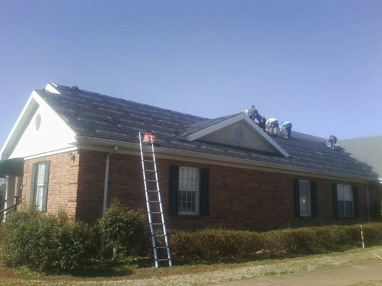 Crew tearing shingles off a brick ranch roof with a ladder set — Emergency Roof Repair work by our crew in San Andreas