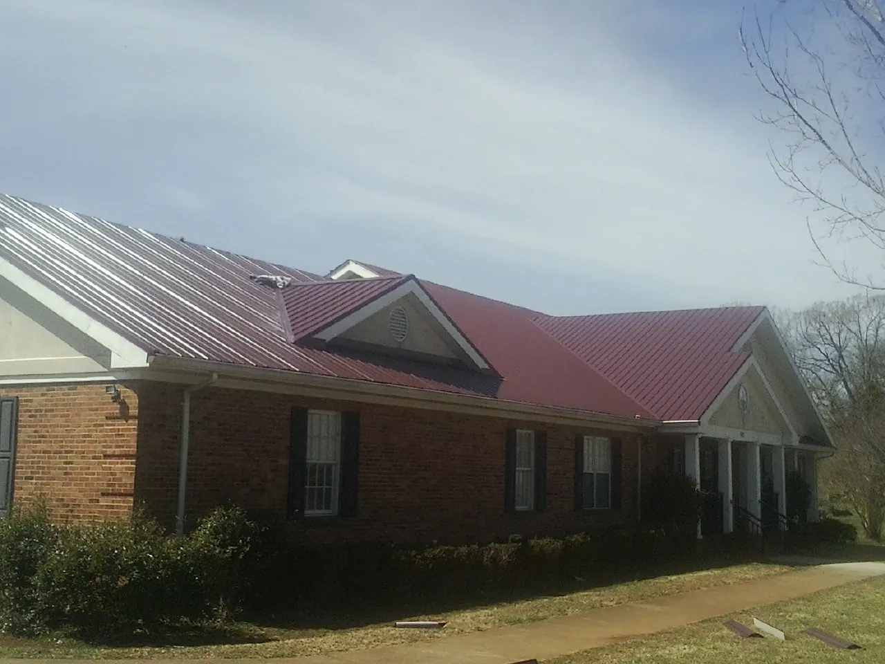 Red metal roof with gabled entries on a long brick building, from a Hail Damage Roof Repair job in San Andreas