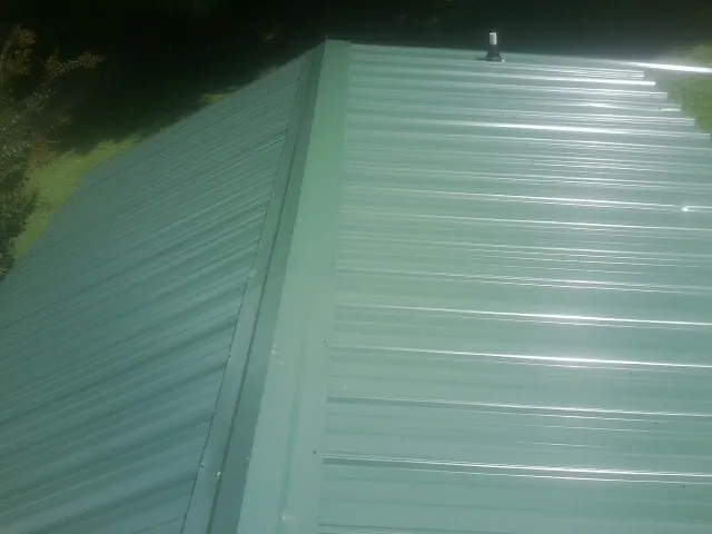 New green metal panels meeting at the ridge of a roof — Flat Roof Repair work by our crew in San Andreas