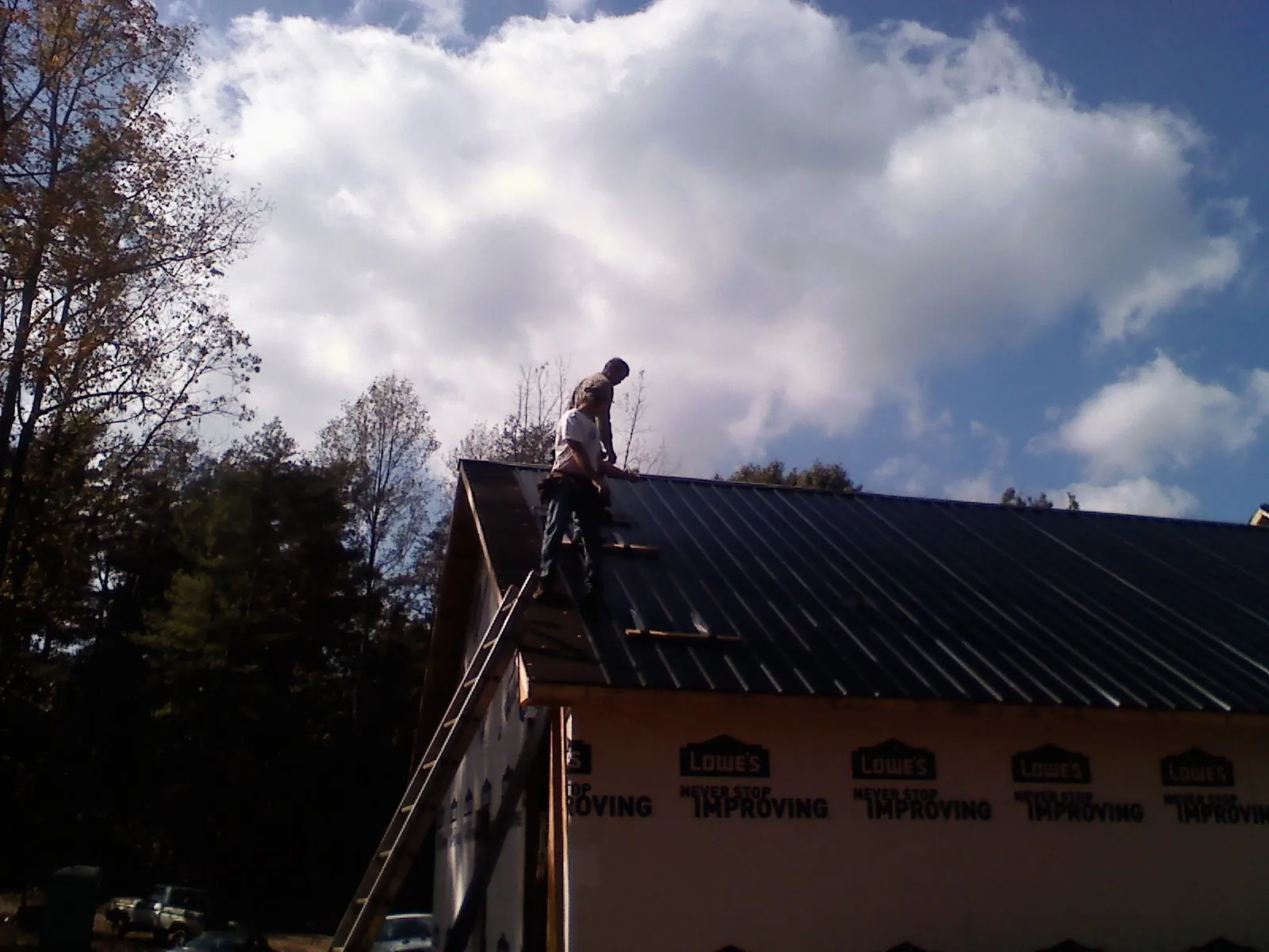 Roofer fastening dark metal panels high against a cloudy sky, from a Roof Inspection job in San Andreas